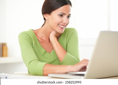 Pretty Latin Lady In Green Shirt Smiling While Working On Her Laptop At Home