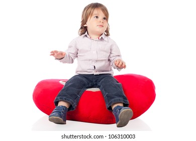Pretty little 2 years old boy wearing shirt and jeans, sitting on a heart shaped red pillow and looking away. High resolution image isolated on white background with copy space. Studio shot