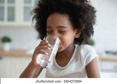 Pretty Little African American Girl Drinking Fresh Water In Kitchen Close Up, Cute Preschool Child Kid Holding Glass Of Pure Mineral Water, Enjoying, Healthy Lifestyle And Refreshment Concept