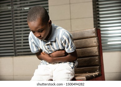 Pretty Little African Boy Sitting On A Bench And Suffering From Strong Stomach Pain