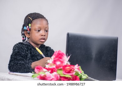 Pretty Little African Girl Child Studying, Reading And Researching Alone With A Black Laptop, Flower And Jotter In Her Front