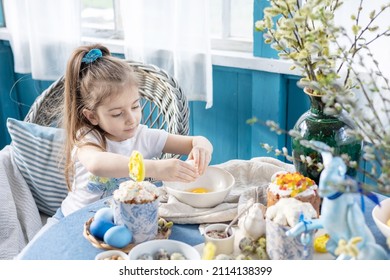 Pretty Little Armenian Girl Helps With Baking For Easter On Veranda On Sunny Spring Day Decorated With Flowers And Easter Decor, Eggs, Cake And Willow Branches, Easter Family Celebration