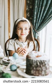 Pretty Little Armenian Girl Helps With Baking For Easter On Veranda On Sunny Spring Day Decorated With Flowers And Easter Decor, Eggs, Cake And Willow Branches, Easter Family Celebration