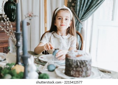 Pretty Little Armenian Girl Helps With Baking For Easter On Veranda On Sunny Spring Day Decorated With Flowers And Easter Decor, Eggs, Cake And Willow Branches, Easter Family Celebration