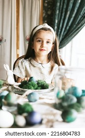 Pretty Little Armenian Girl Helps With Baking For Easter On Veranda On Sunny Spring Day Decorated With Flowers And Easter Decor, Eggs, Cake And Willow Branches, Easter Family Celebration