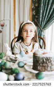 Pretty Little Armenian Girl Helps With Baking For Easter On Veranda On Sunny Spring Day Decorated With Flowers And Easter Decor, Eggs, Cake And Willow Branches, Easter Family Celebration