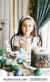 Pretty Little Armenian Girl Helps With Baking For Easter On Veranda On Sunny Spring Day Decorated With Flowers And Easter Decor, Eggs, Cake And Willow Branches, Easter Family Celebration