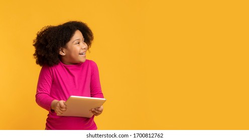 Pretty Little Black Girl Holding Digital Tablet And Looking Aside At Copy Space Over Yellow Background, Panorama