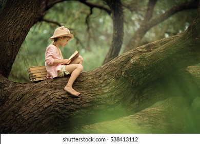 A Pretty Little Blonde Girl In A Straw Hat Reading A Book On A Large Spreading Tree. Children And Science.