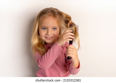 Una linda niña con grandes ojos azules y un peine en la mano. El niño peina el pelo rebelde. Una niñita linda está jugando con un cepillo de pelo.
