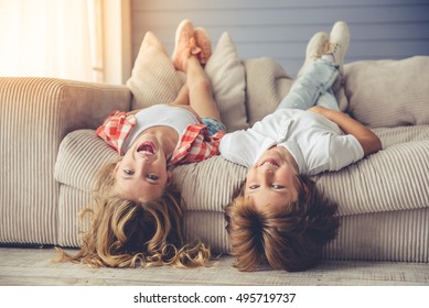 Pretty little girl and boy are lying on their backs on sofa, looking at camera and smiling while playing at home - Powered by Shutterstock