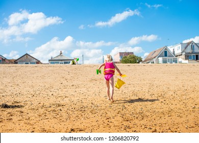 A pretty little girl carrying a yellow bucket walking on the beach towards the sea wearing a pink swimming costume and wearing a life jacket, buoyancy aid for safety - Shutterstock ID 1206820792