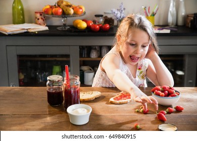 Pretty little girl eating strawberries and jam in a kitchen - Shutterstock ID 649840915