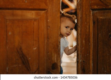 a pretty little girl hiding behind a large wooden door looking in the gap between them. Selective focus, noise effect