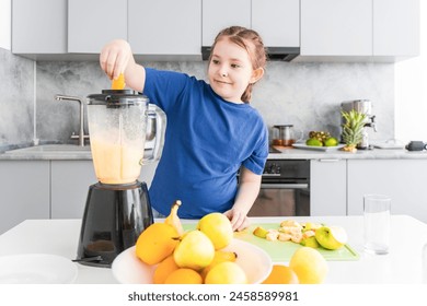 Pretty little girl making a fruit cocktail in the kitchen. A teenage girl puts fruit in a blender. Selected Focus. High quality photo - Powered by Shutterstock