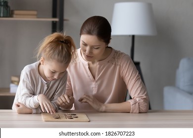 Pretty little girl and mother playing interesting wooden board game, checkers on weekend, sitting at table at home, focused young woman and preschool daughter spending leisure time together - Powered by Shutterstock