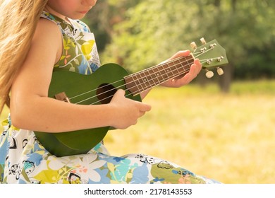 
Pretty Little Girl Playing The Ukulele. The Child Plays Music.