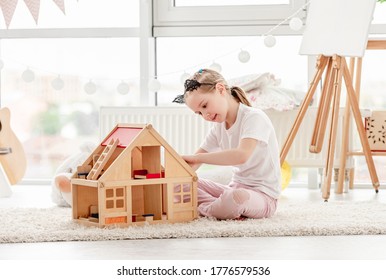 Pretty Little Girl Plays With Wooden Dollhouse In Children's Room