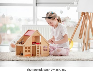 Pretty Little Girl Plays With Wooden Dollhouse In Children's Room