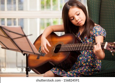 Pretty little girl practicing some new sound on a guitar at home - Powered by Shutterstock