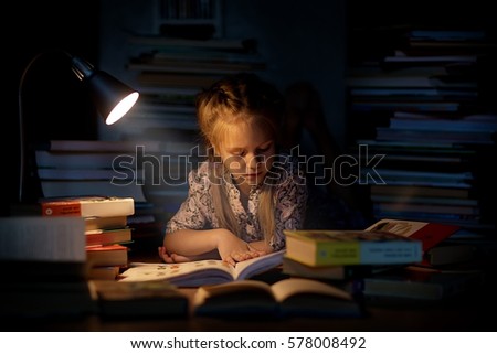 A pretty little girl reading a book on the floor under the lamp. Children and education.