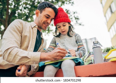 A Pretty Little Girl In A Red Cap Drawing With Her Dad Outdoor After School. Father Enjoying The Time Together With His Child Outside. Daddy And Daughter Share Love. Father's Day.