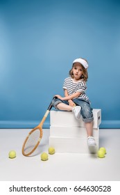 Pretty Little Girl Sitting On White Boxes And Holding Tennis Raquet  