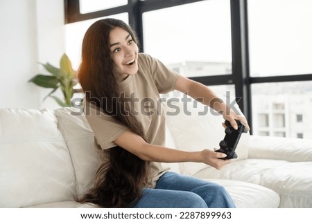 Pretty long hair woman playing online video game console sitting on the couch in front of tv in modern living room.