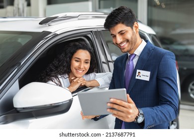 Pretty Long-haired Brunette Lady Sitting Inside Brand New Comfy White Car, Having Conversation With Cheerful Sales Assistant, Looking At Digital Tablet In Dealer Hands, Checking Auto Features