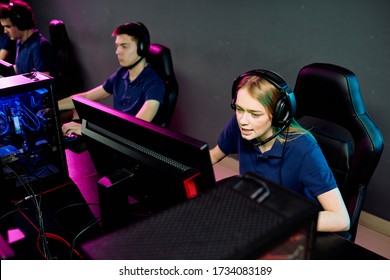 Pretty Long-haired Girl In Headset Talking To Someone While Sitting In Front Of Computer Monitor And Looking At Screen During Video Game