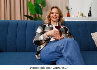 Pretty Mature Woman With Glass Of Red Wine Sitting On Sofa In Living Room