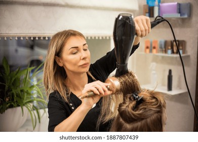 Pretty mature woman hairdresser enjoying working in beauty salon and blowdrying hair of client