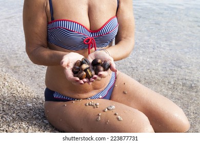 Pretty Middle Aged Woman Holding Roasted Chestnuts On The Sunny Beach, Whilst Standing In Sea, Wet Skin With Goosebumps 