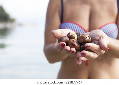 Pretty Middle Aged Woman Holding Roasted Chestnuts On The Sunny Beach, Whilst Standing In Sea, Wet Skin With Goosebumps 