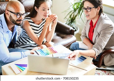 Pretty middle-aged interior designer sharing ideas with her clients while having meeting in cozy boardroom, they listening to her with interest