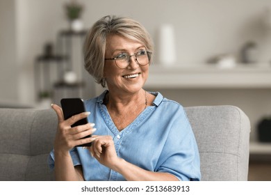 Pretty middle-aged woman in glasses looking away holding smartphone smile, resting on sofa at home, making call, browse wireless internet, search information, spend free time online on leisure indoors - Powered by Shutterstock