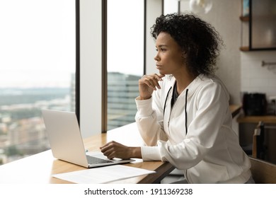 Pretty Millennial Black Woman Freelancer Sit By Laptop In Modern Flat Think On Problem Look At Large Window With Splendid City View. Pensive Young Afro Lady Take Break In Online Work From Home Office