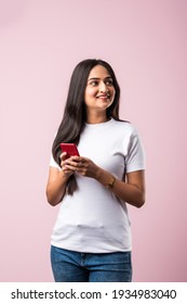 Pretty Millennial Indian Girl Isolated On Pink Studio Background Text Messaging On Cell Phone Or Using Smartphone With Wireless Connection