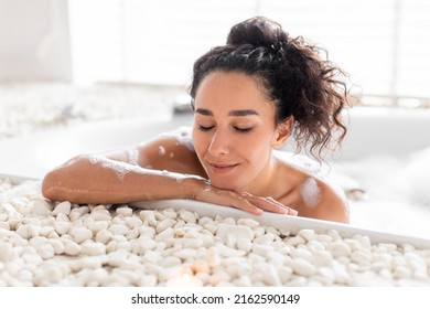 Pretty Millennial Woman Lying In Foamy Bathtub With Closed Eyes, Enjoying Bubble Bath At Hotel. Sexy Young Female Pampering Her Body Indoors. Home Spa And Relax On Weekends