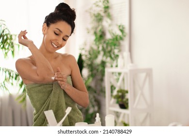 Pretty Millennial Woman In Towel Applying Soothing Cream On Elbows In Front Of Mirror At Home, Empty Space. Millennial Female Pampering Herself At Bathroom. Dry Skin Treatment