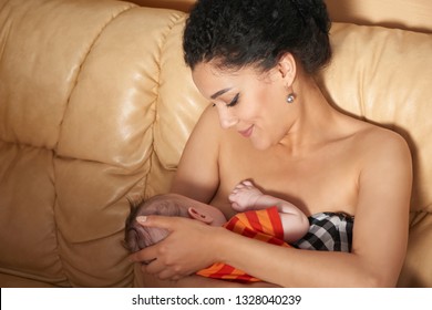 Pretty mixed race african american - caucasian woman breastfeeding her newborn baby on sofa
