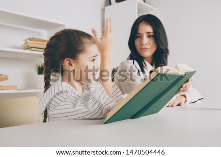Pretty mother with cute daughter sitting with book in the room at home.