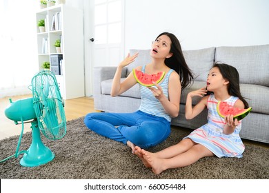 Pretty Mother With Cute Little Daughter Feeling Very Hot At Summer Day And Eating Watermelon Blowing Electric Fan Cool Wind.