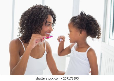 Pretty mother with her daughter brushing their teeth at home in the bathroom