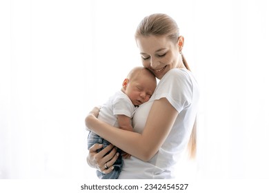 Pretty mother holding cute baby in hands standing by the white wall, panorama with free space - Powered by Shutterstock