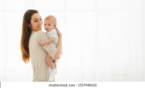 Pretty Mother Holding Cute Smiling Baby In Hands Standing Near Window At Home, Panorama With Free Space