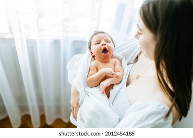 Pretty mother holding her newborn baby yawning daughter on arms. Concept of single parent, love, care and family, newborn baby girl, new life concept.