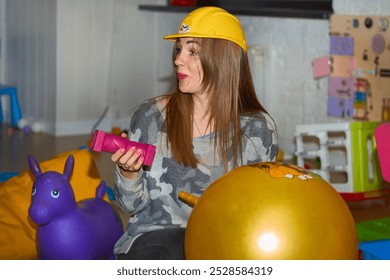 Pretty nanny in safety helmet playing with children in playroom in kindergarten - Powered by Shutterstock