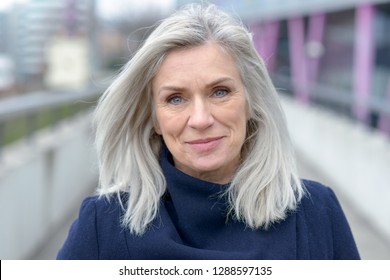 Pretty natural grey blond middle-aged woman with a lovely smile looking into the lens as she stands on an outdoor pedestrian walkway in town - Shutterstock ID 1288597135