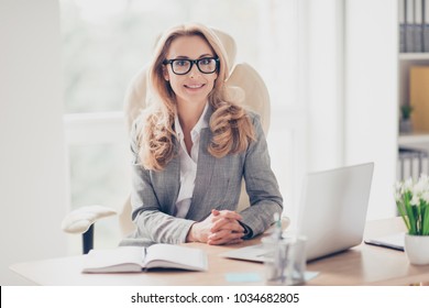 Pretty, nice, cute, perfect woman sitting at her desk on leather chair in work station, wearing glasses, formalwear, having laptop and notebook on the table, looking at camera